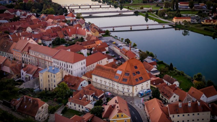 Pogled iz zraka na Ptuj ob Dravi; v ospredju stavba Knjižnice Ivana Potrča Ptuj in mostovi čez reko.
